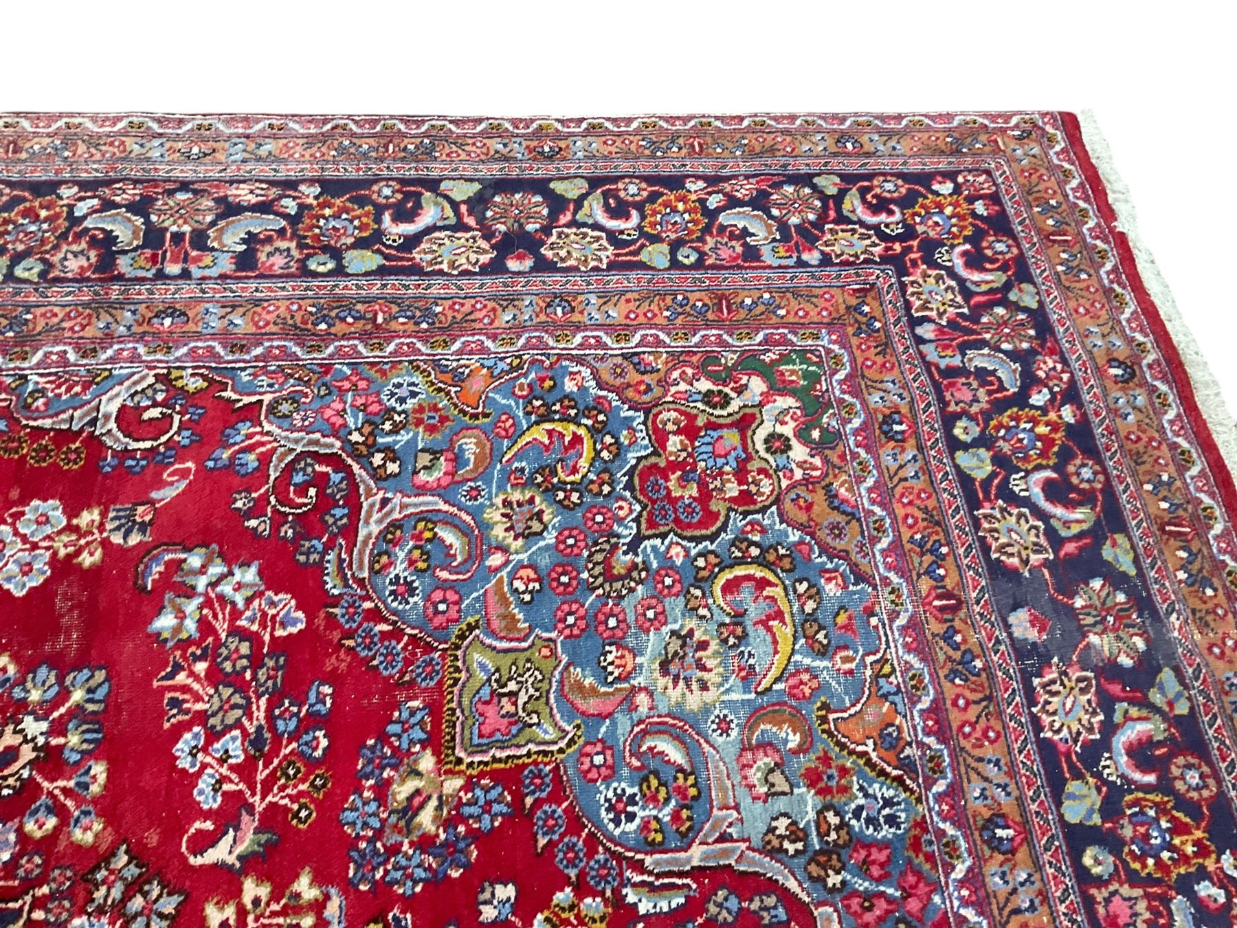 Large Persian Kashan crimson ground carpet, the busy field decorated with a central floral pole medallion surrounded by stylised plant motifs and palmettes with contrasting indigo spandrels, the guarded border decorated with repeating connected foliate designs