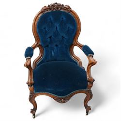 Victorian walnut framed open armchair, curled leaf carved cresting rail over scrolled and shaped arms, upholstered in buttoned blue velvet fabric, on cabriole feet