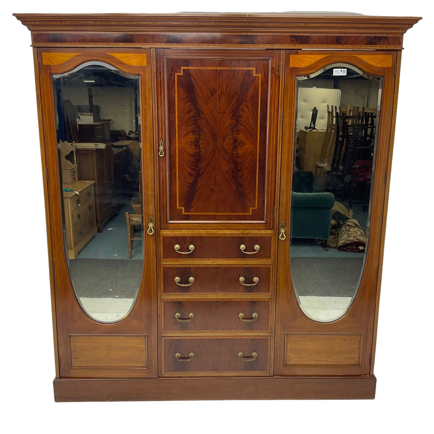 Edwardian inlaid mahogany combination wardrobe, projecting moulded cornice over figured frieze with satinwood banding, the central section fitted with cupboard over four long drawers, figured matched veneers and satinwood bands, flanked by two full height compartments enclosed by bevelled shield shaped mirror doors, satinwood fan inlaid spandrels, on moulded skirt base 