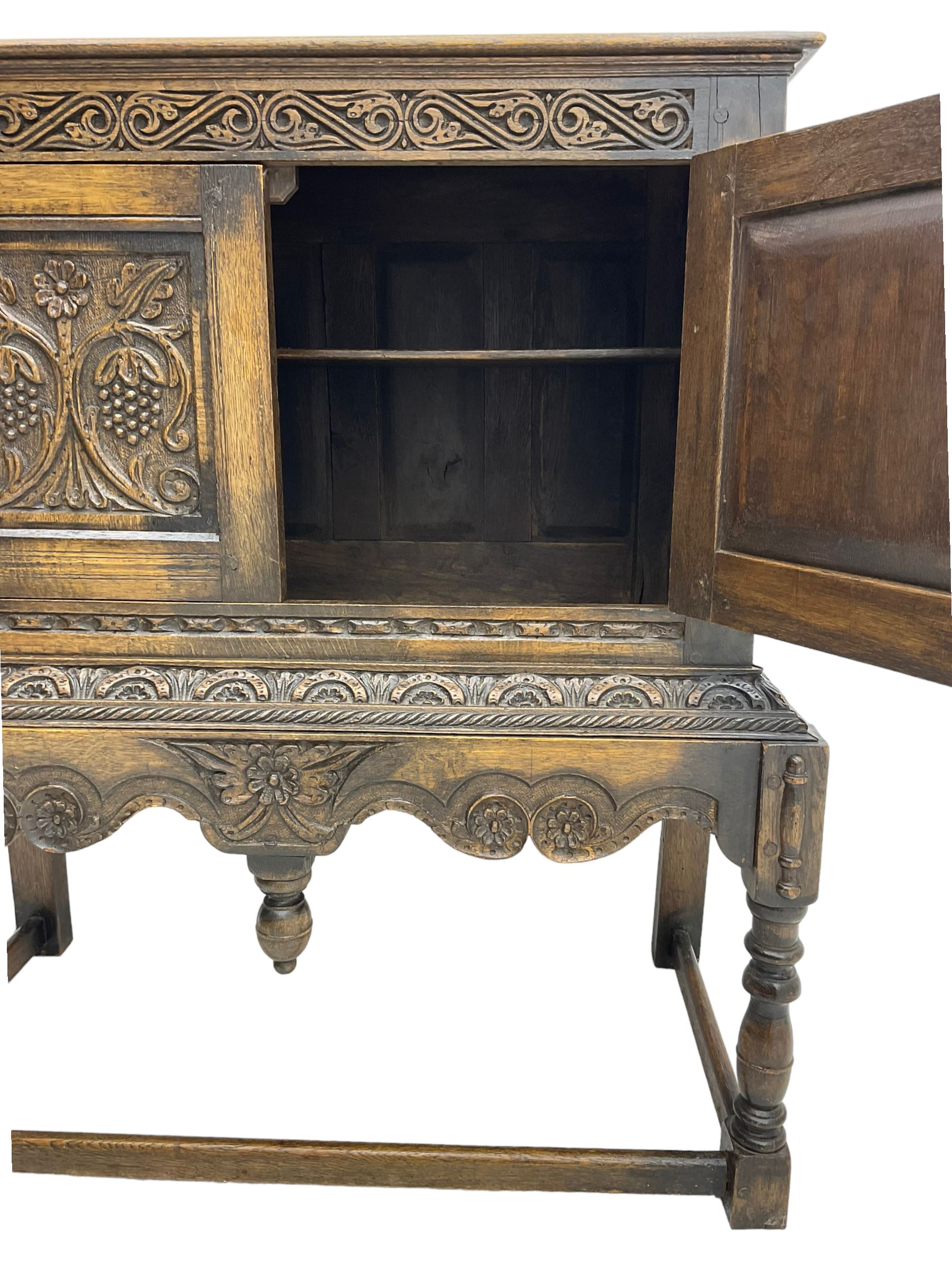 Jacobean Revival carved oak cupboard, moulded rectangular top over S-scroll carved frieze and two doors, the panelled doors carved with stylised plant motifs, on stand decorated with lunettes and shaped apron with hanging turned pendant, on turned supports united by stretchers 