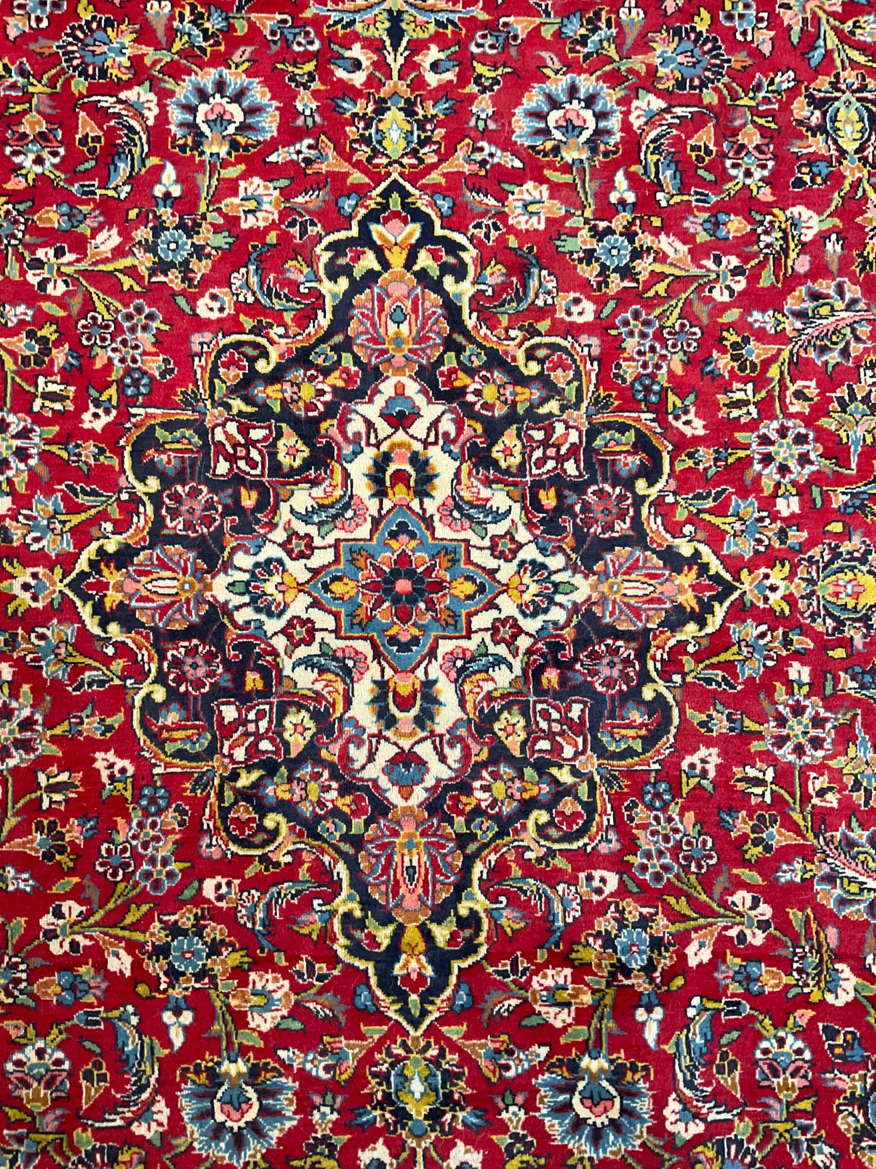 Persian Kashan crimson ground carpet, floral design central medallion surrounded by trailing leafy branches and stylised plant motifs, multi-band border with repeating floral design