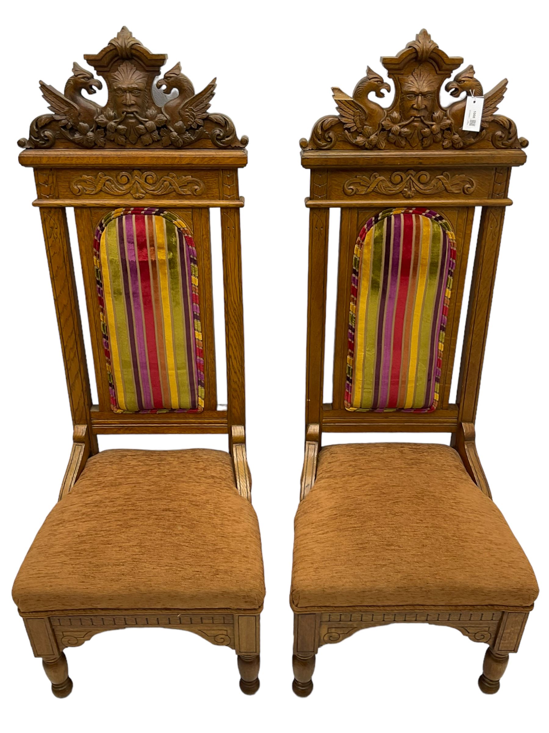 Set of six 20th century Carolean design oak high back chairs, the pediment carved with dragons and central Green Man mask with trailing foliage, the backs upholstered in striped fabric, on turned front supports