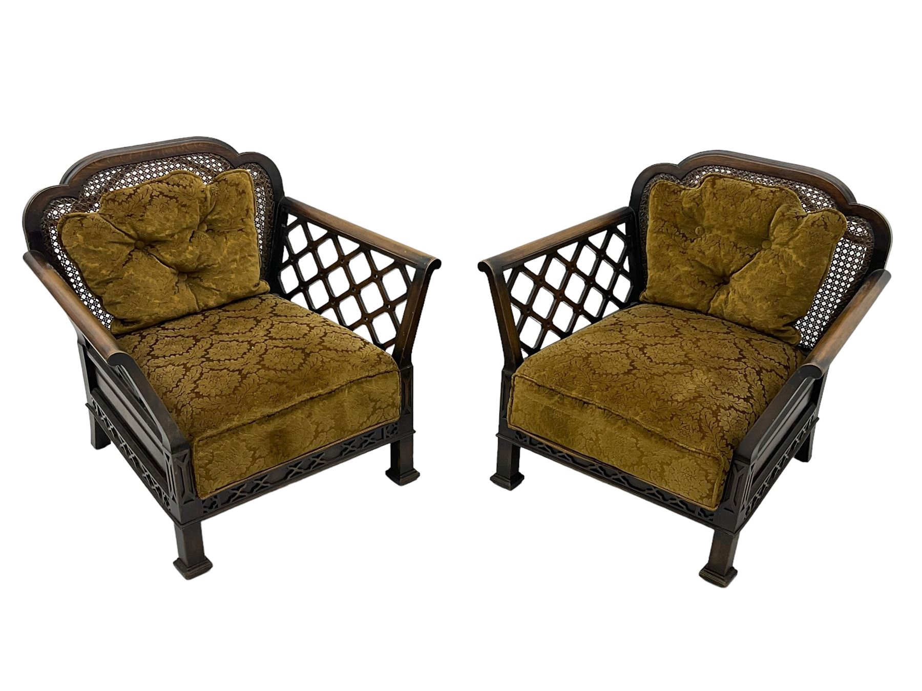 Early 20th century three-piece bergère suite - three seat sofa (W177cm, H82cm, D75cm); pair of matching armchairs (W84cm); single caned back with 'cock-pen' panelled arms, upholstered in foliate pattern fabric, blind fretwork lower frieze over square feet 