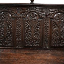 18th century oak settle or bench, moulded cresting rail with globular finials over five panel back, each stepped arch panel carved with stylised leaf decoration, hinged box seat over S-scroll foliate frieze and two panels carved with scrolling pattern, panelled sides, on stile supports terminating to turned feet 