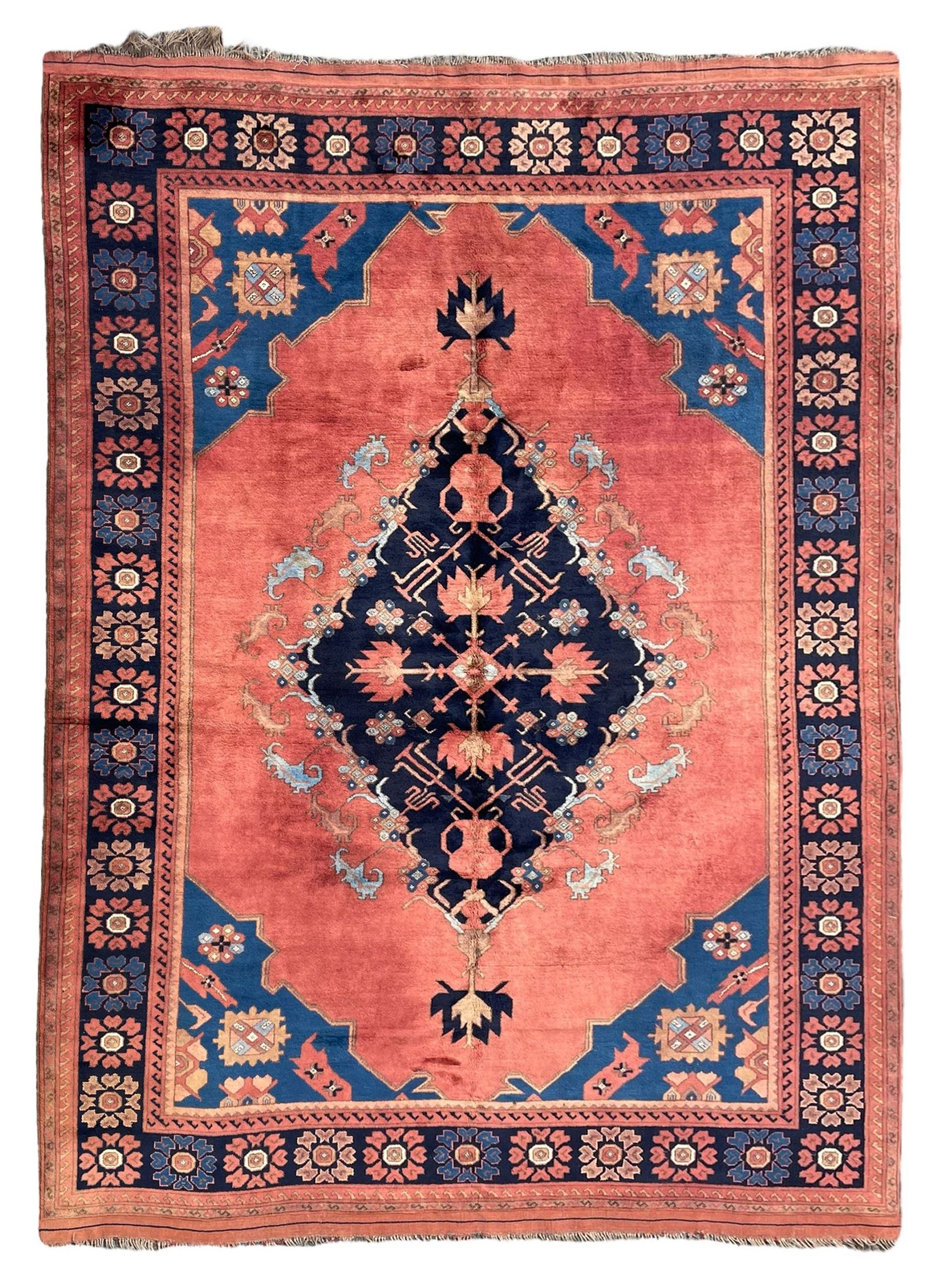 Afghan rust ground carpet, large central lozenge medallion decorated with stylised plant motifs, running water guard stripes enclosing indigo ground border decorated with stylised flower heads