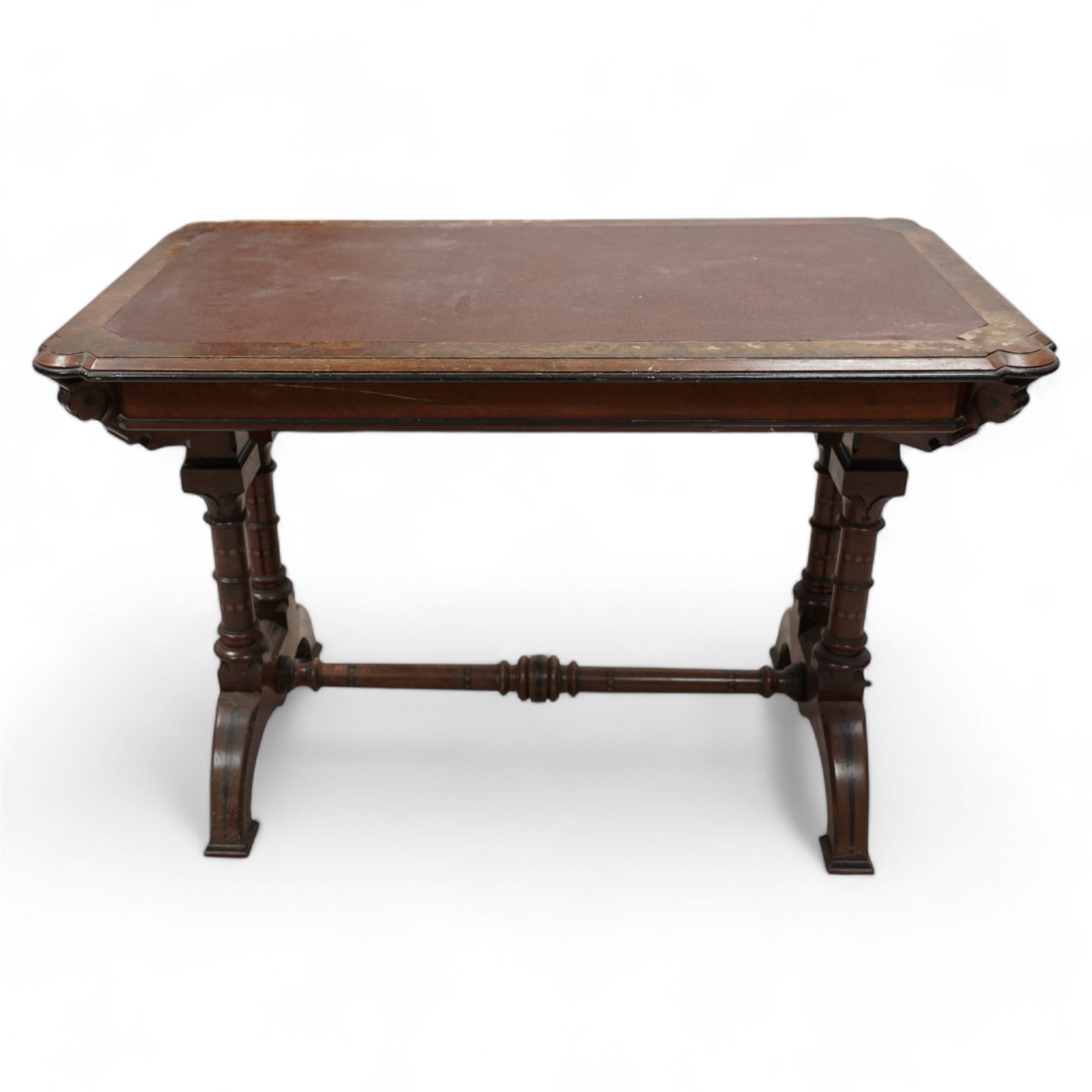 Late 19th century Aesthetic Movement inlaid walnut library table, shaped rectangular top with moulded and banded edge, inset with oxblood leather writing surface, fitted with two frieze drawers, raised on ring turned twin-pillar end supports with carved acanthus capitals terminating to arched supports with ebony inlay, united by turned stretcher 