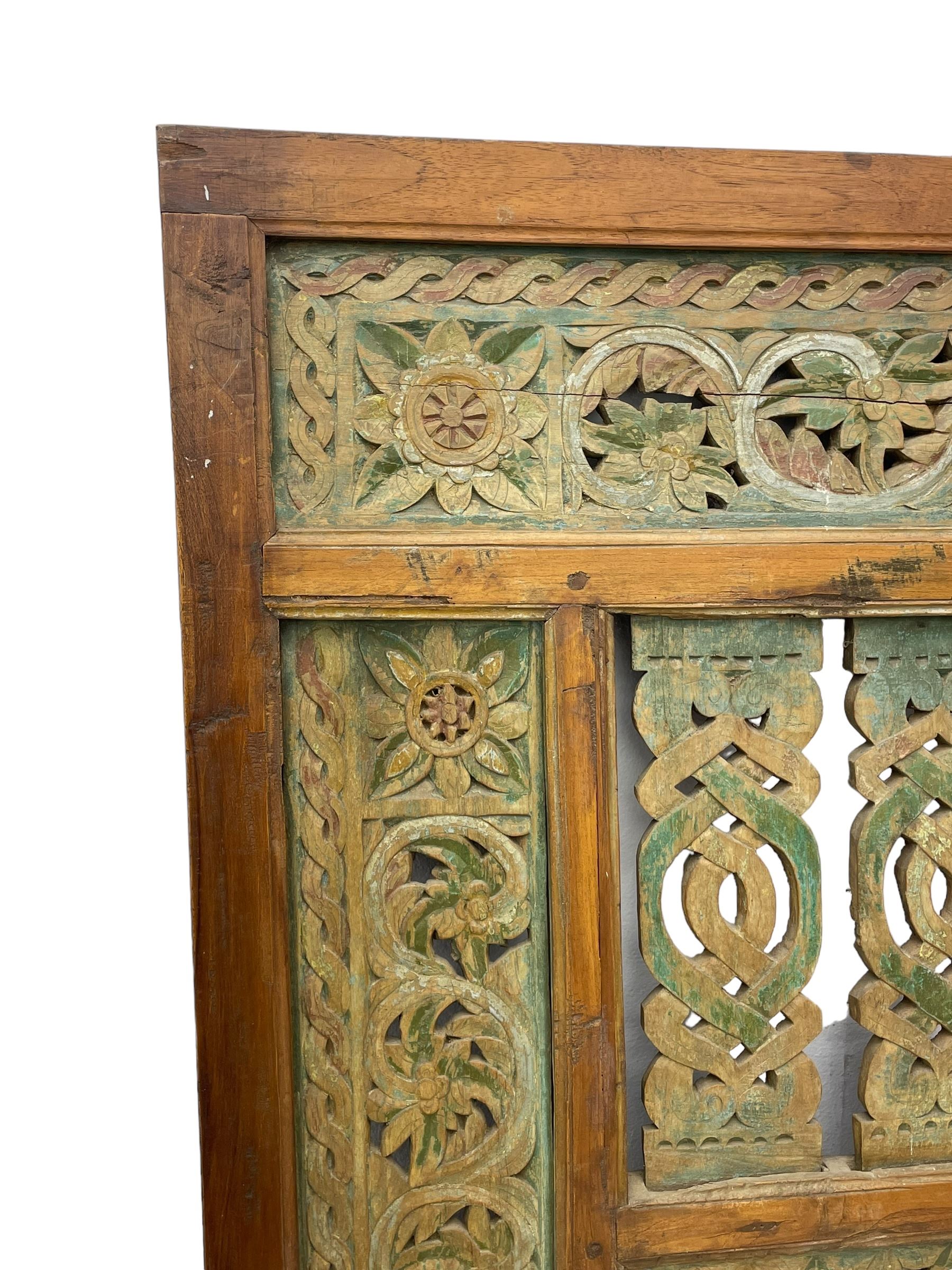 Early 20th century Javanese teak and hardwood door panel or room divider, rectangular panelled form with moulded frame and pegged construction, carved and pierced with scrolling decoration and flower head motifs, shaped and pierced splats with interlocking pattern