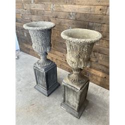 Pair of Georgian design cast stone garden urns, egg and dart rim with raised floral motifs, pedestal base terminating on square plinth, raised on square block plinth