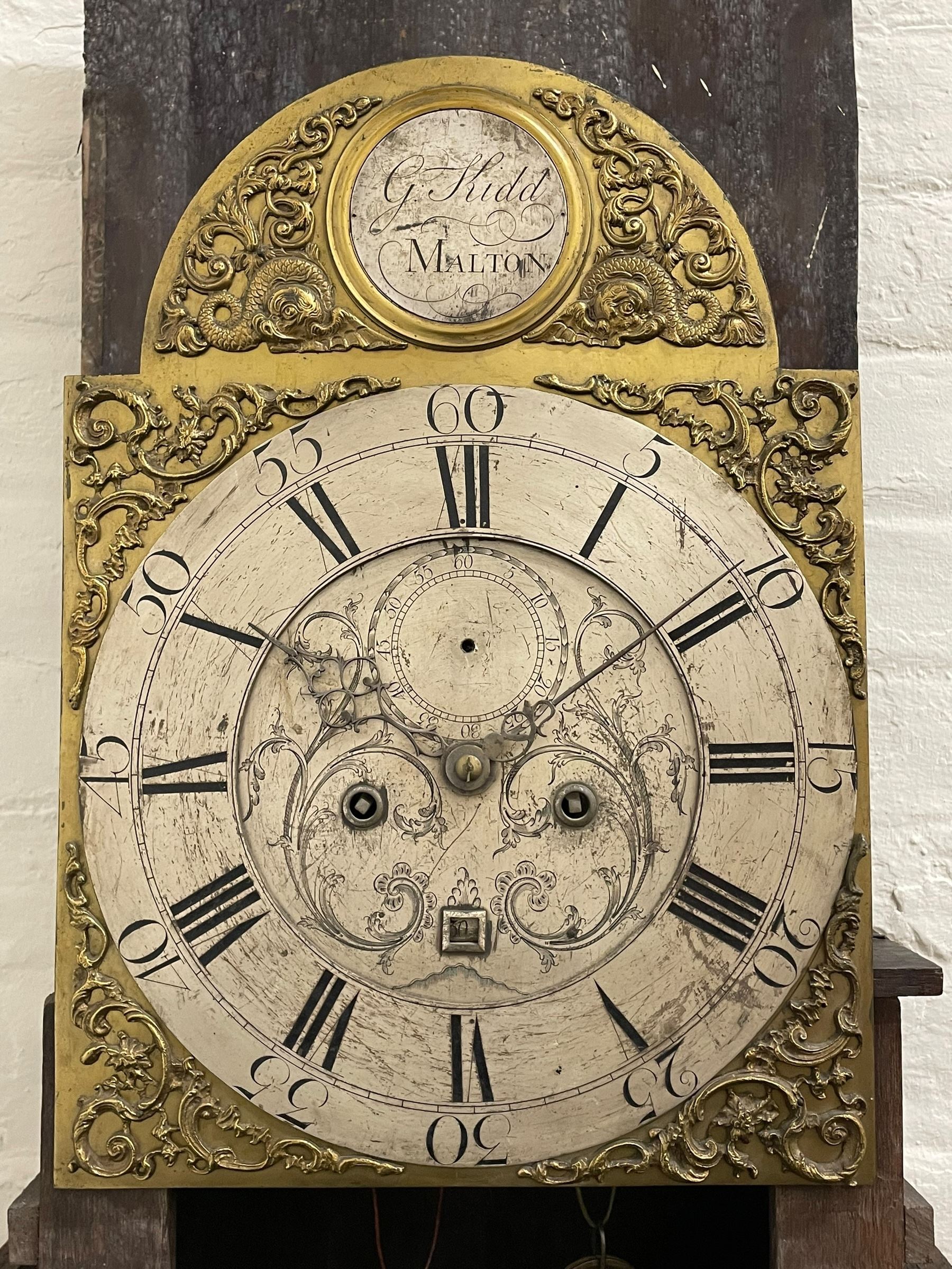 Gilbert Kidd of Malton (North Yorkshire) - late 18th century oak 8-day longcase clock c1780,  with a tall double caddy top and later brass ball and spire finials, break arch hood door beneath with attached pilasters and wooden capitals,  plain trunk with a long flat topped door, raised on a square plinth with applied skirting,  brass break arch dial with the makers name to the silvered boss in the break arch, engraved and silvered dial centre and chapter ring, with cast spandrels and matching steel hands, subsidiary seconds dial and square calendar aperture, dial pinned directly to a rack striking movement with a recoil anchor escapement, sounding the hours on a cast bell. With pendulum and weights.
The Kidd family were a prolific family of provincial clockmakers working in Malton from the mid 18th century until the early 19th century. Many of their clocks are simply signed 