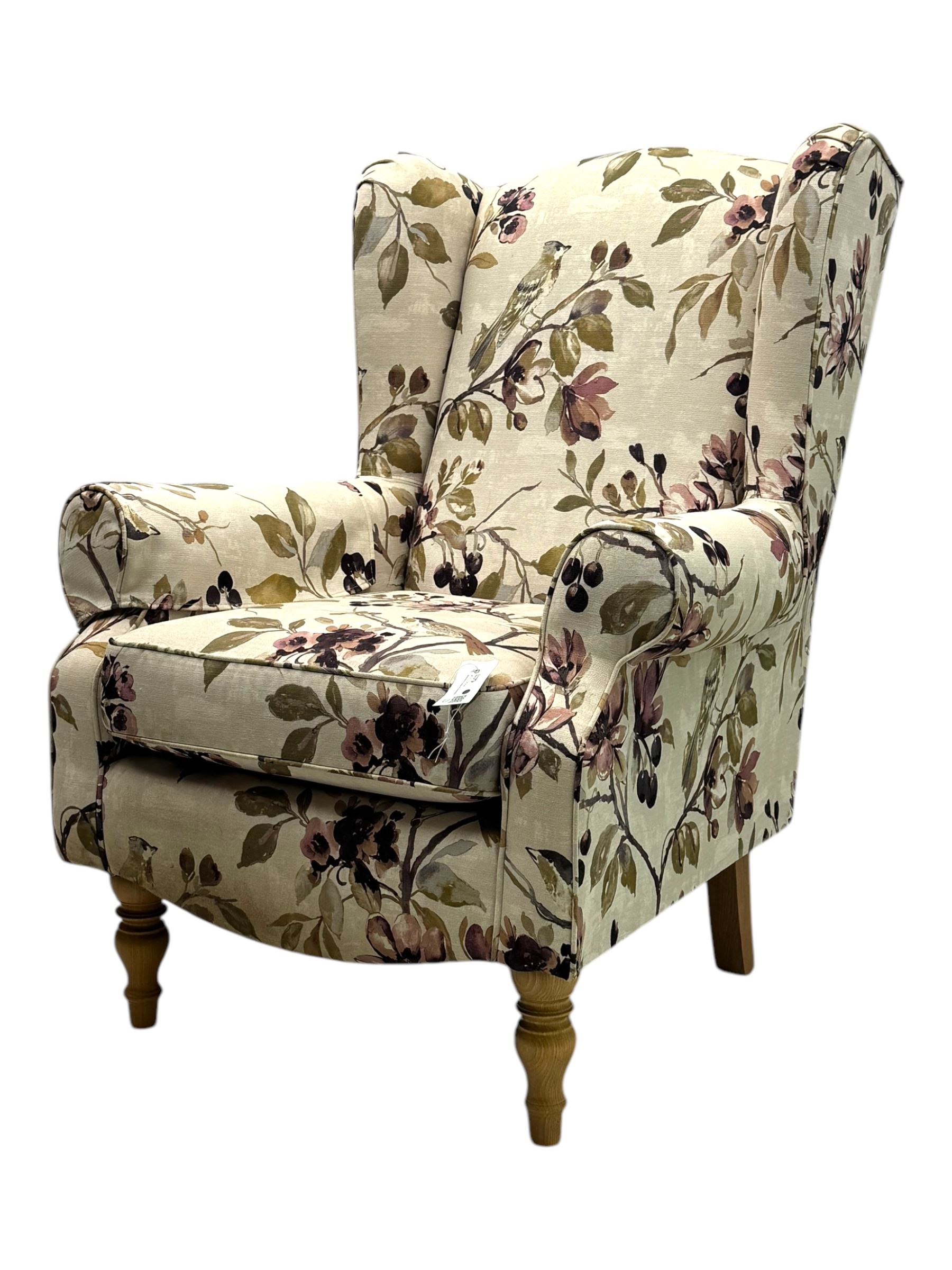 Hardwood-framed wingback armchair, upholstered in cream floral pattern fabric, on turned front feet