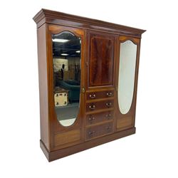 Edwardian inlaid mahogany combination wardrobe, projecting moulded cornice over figured frieze with satinwood banding, the central section fitted with cupboard over four long drawers, figured matched veneers and satinwood bands, flanked by two full height compartments enclosed by bevelled shield shaped mirror doors, satinwood fan inlaid spandrels, on moulded skirt base 