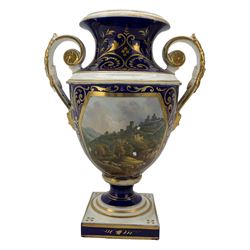 Early 19th century Derby porcelain urn, the reserve painted with a pastoral landscape and castle in the distance, with twin scroll and mask handles, upon a square pedestal base, H23cm, together with a Derby shell-shaped dish, centrally hand painted with a landscape scene titled 'In North Wales', within a cobalt blue and gilt border, L25cm (2)