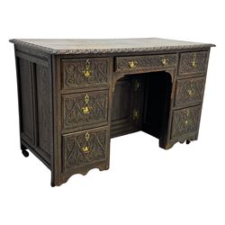 Victorian carved oak kneehole desk, the rectangular top with carved edge, above central drawer with carved front and brass handles, central kneehole with cupboard door, flanked by two banks of three graduating drawers each with similarly carved decoration, on shaped plinth base with castors