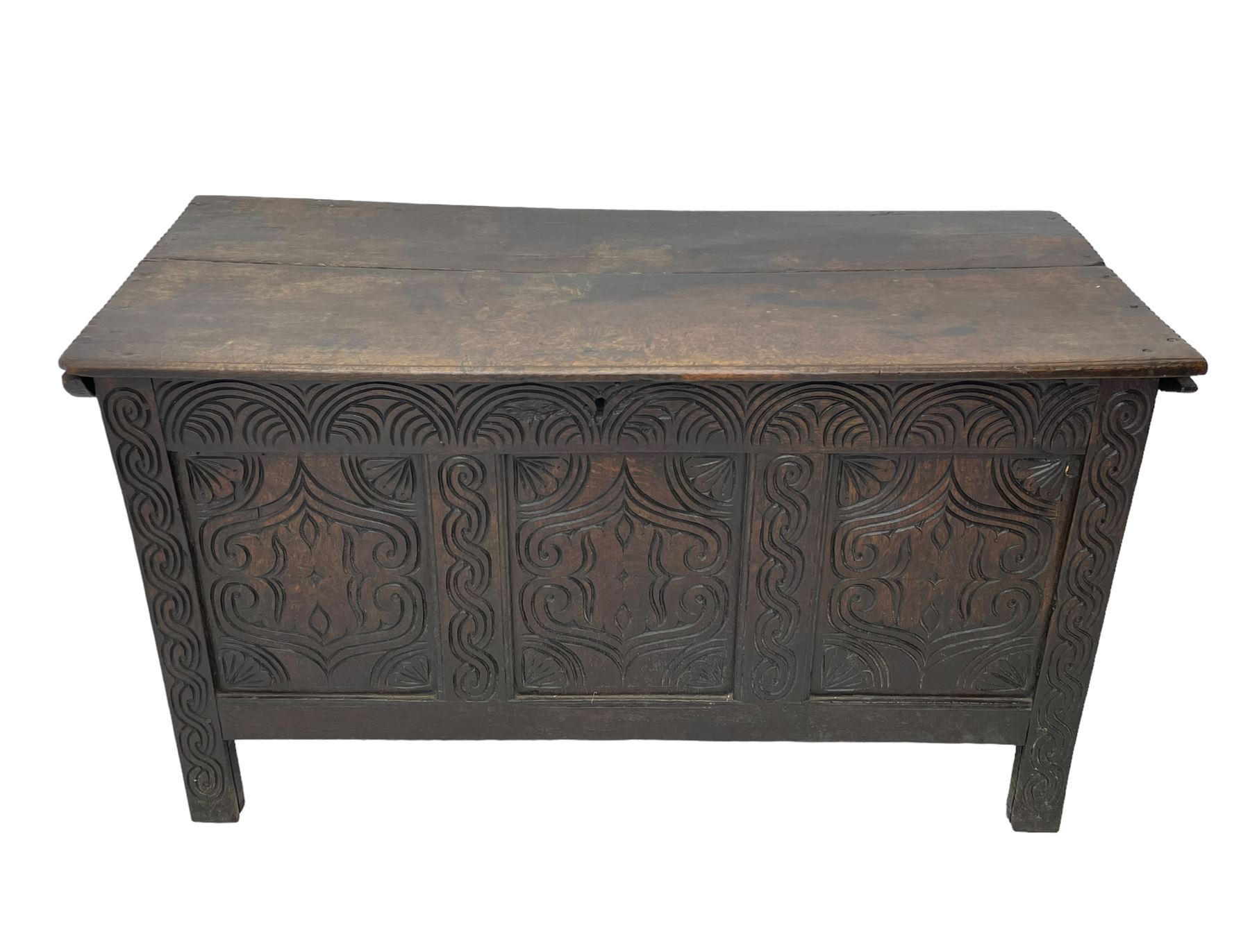 18th century oak blanket box, moulded and chip carved hinged lid, lunette carved cresting rail over triple panelled front carved with stylised leaf and scroll decoration, interlocking S-scroll carved upright rails, panelled sides and back, on stile supports 