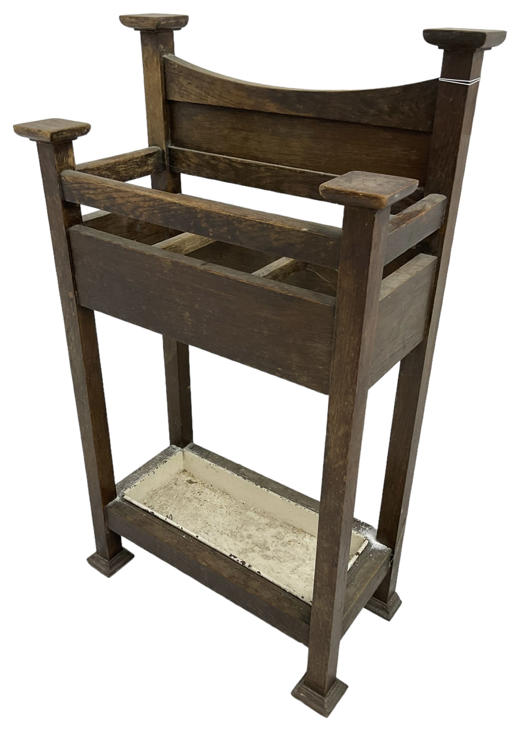 Early 20th century Arts & Crafts oak stick stand, panelled back over three divisions, fitted with metal drip tray, on square supports