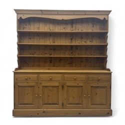 Large traditional pine dresser, shaped cornice over three open shelves, base fitted with four drawers above four panelled cupboards, each with turned wooden knobs, on plinth base