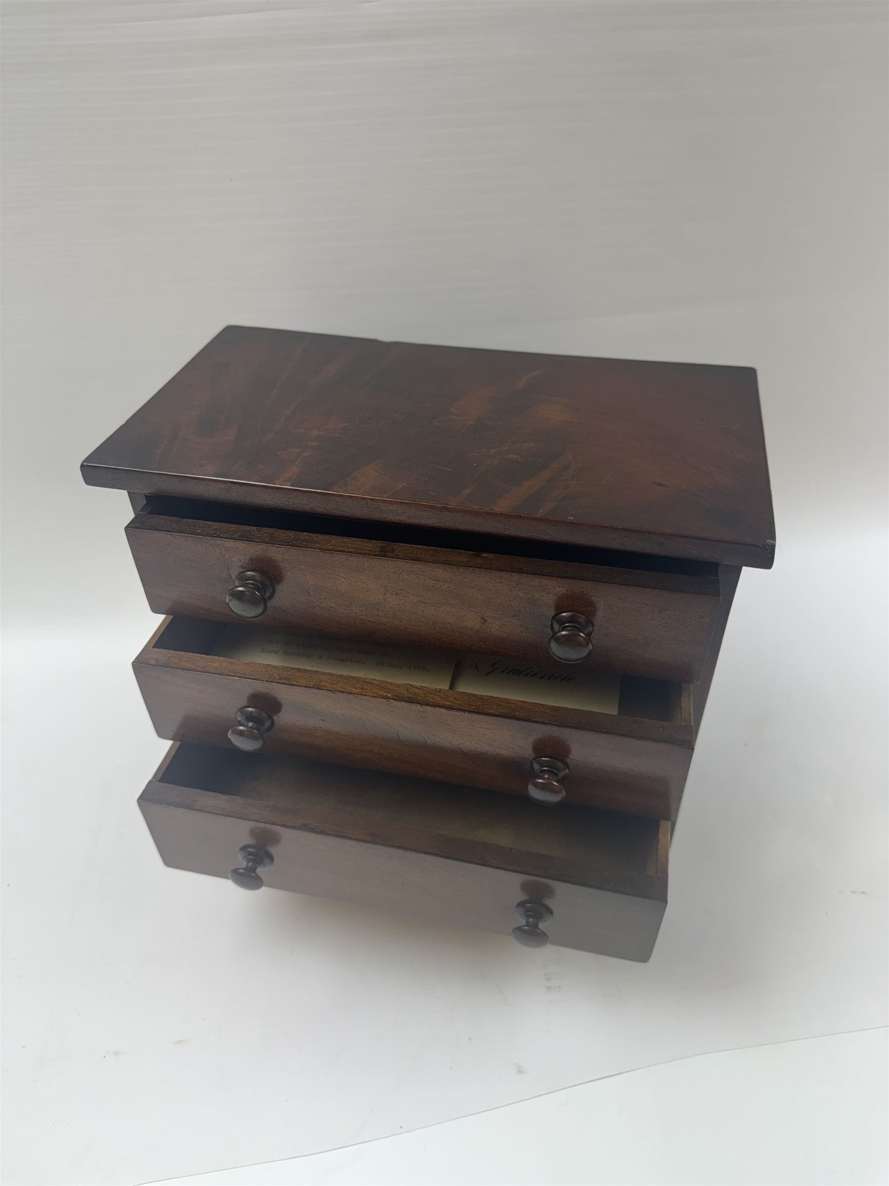 19th century mahogany miniature chest of drawers, with three graduating drawers, each with wooden handles, with inlaid shaped front and upon four bracket feet, H24cm