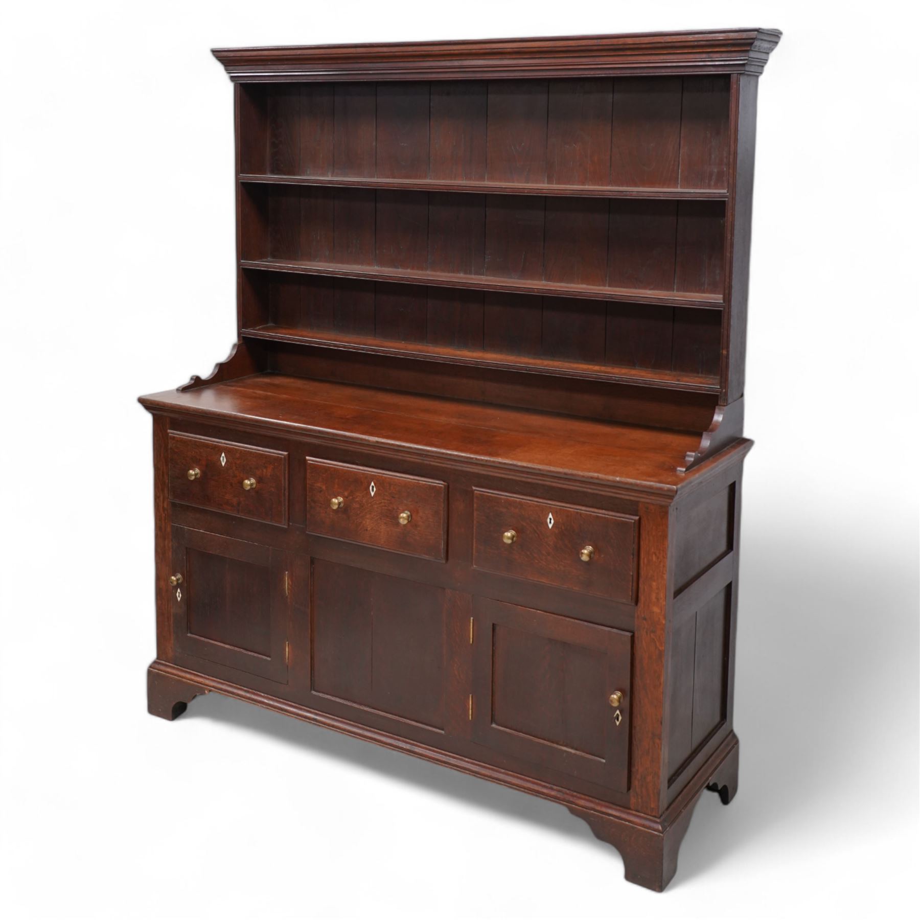 Late 18th century oak dresser, moulded cornice over three-tier plate rack, the base fitted with three drawers and two cupboards, enclosed by two panelled doors, on bracket feet, bone lozenge escutcheons 