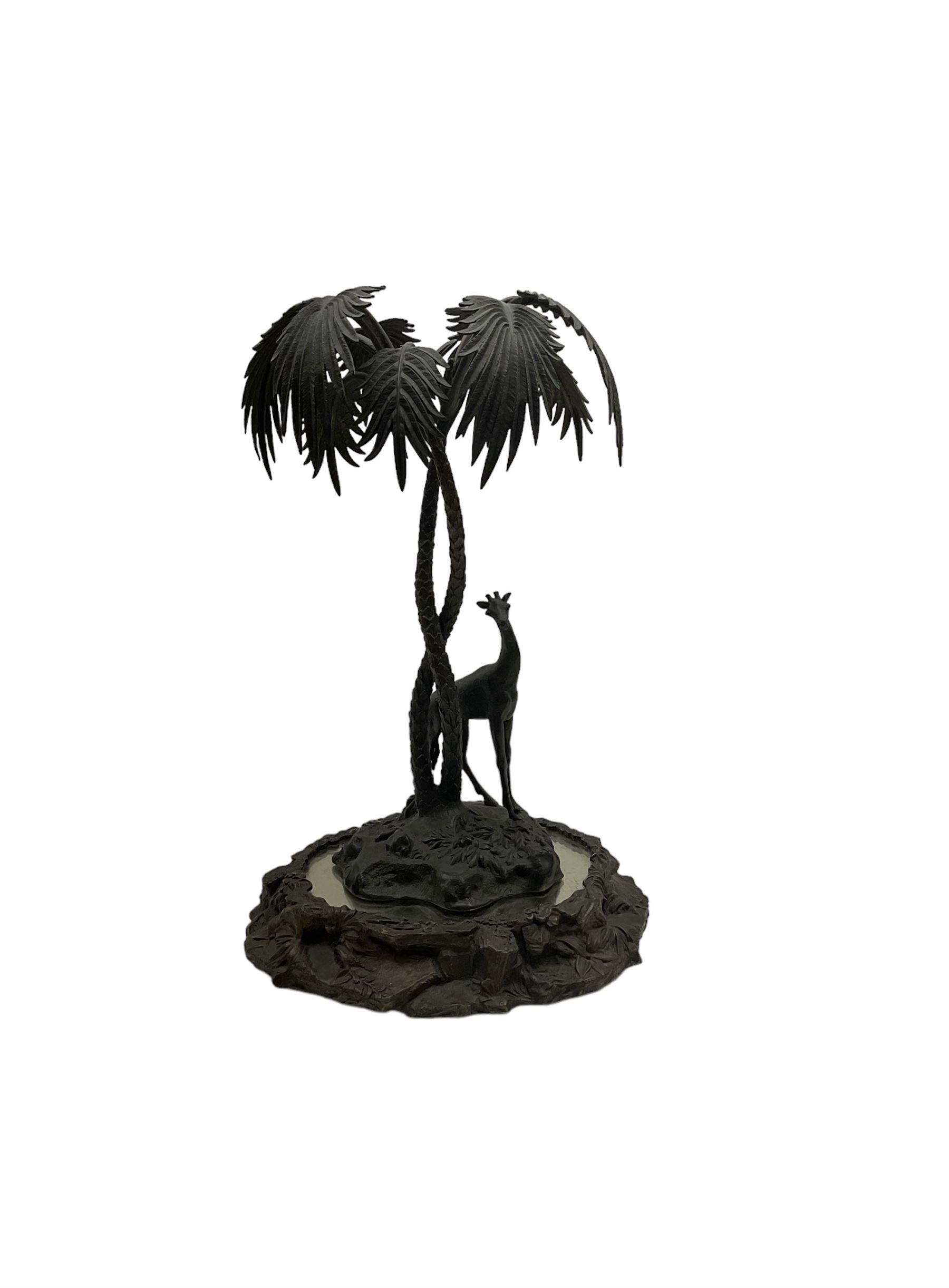 Sculpture of a giraffe under a palm tree upon a mirrored base, H48cm