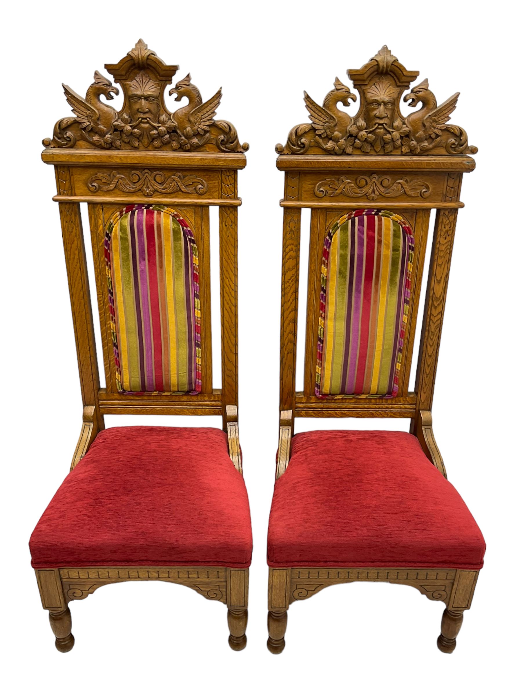 Set of six 20th century Carolean design oak high back chairs, the pediment carved with dragons and central Green Man mask with trailing foliage, the backs upholstered in striped fabric, on turned front supports