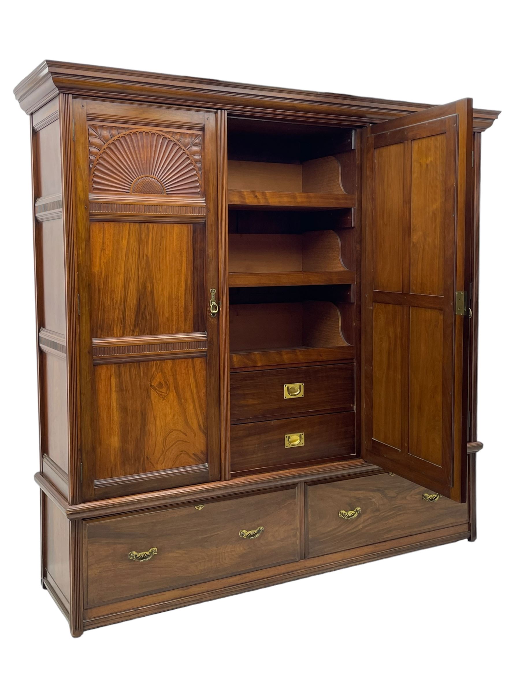 Late Victorian walnut triple wardrobe, projecting moulded cornice over central bevelled mirror door and flanking panelled doors, the top panels carved with fluted fans and stylised leaf motifs, the interior fitted with three linen slides, two drawers and hanging space, two long drawers to base, reed moulded uprights and vertical fluted horizontal rails 