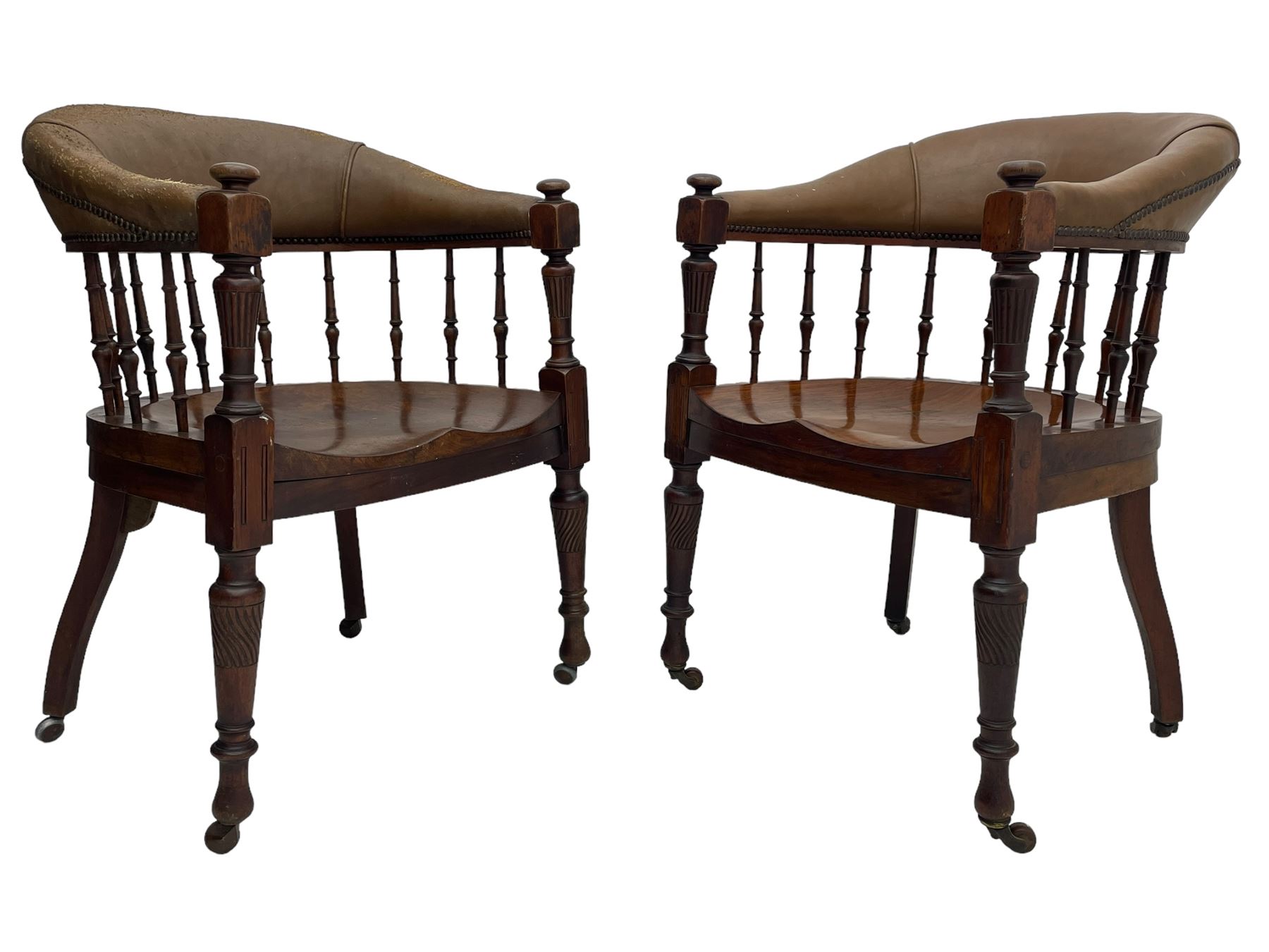 Pair of late Victorian walnut tub-shaped elbow chairs, the cushioned cresting rail upholstered in leather on spindle turned supports, dished saddle seat on turned supports