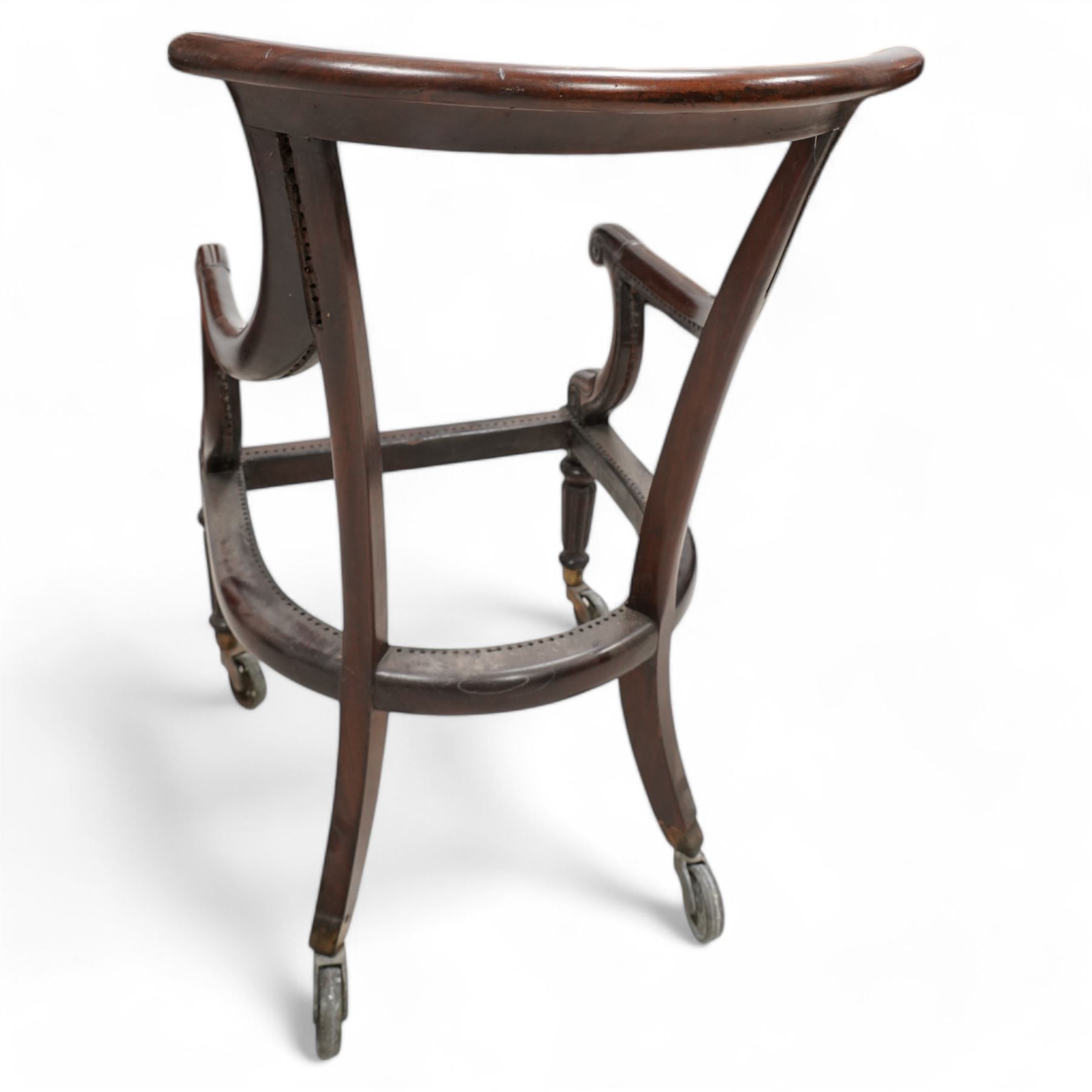 Possibly Gillows - Regency mahogany library chair frame, curved and rolled cresting rail over sweeping arms with lappet and scroll carved terminals, on turned and reed carved supports, brass cups and spoked wheel castors 