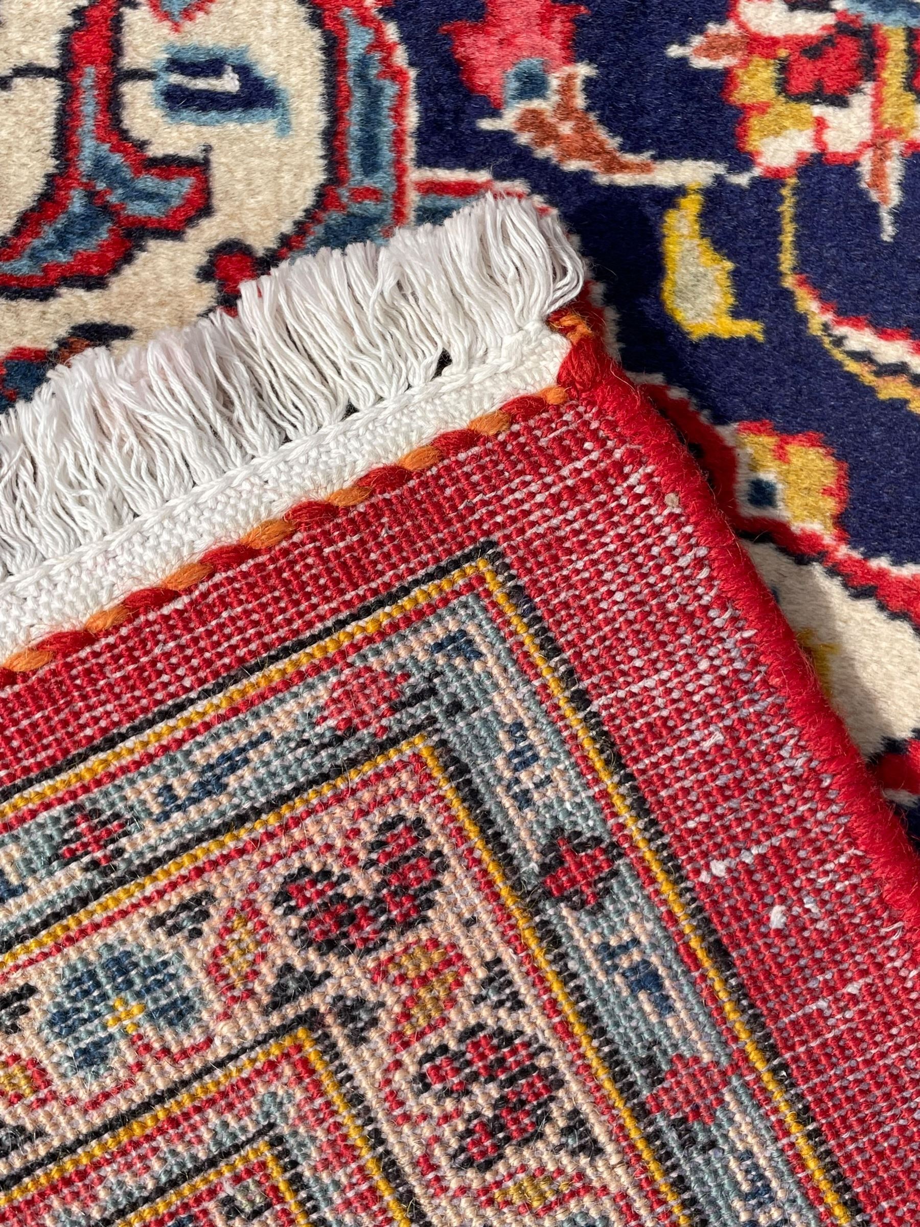 Persian Kashan crimson ground rug, overall arabesque design, the field decorated with swirled leafy branches and palmettes, indigo ground border decorated with repeating pattern, within guard stripes 