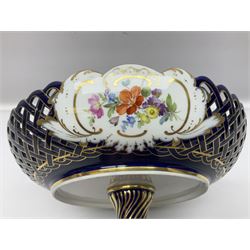 Meissen style pedestal dish, with central panel depicting a trading scene in a harbour setting, the bowl with openwork lattice sides divided by three hand painted floral panels, upon a blue ground with gilt detailing, upon a fluted knopped pedestal and circular foot, H22cm