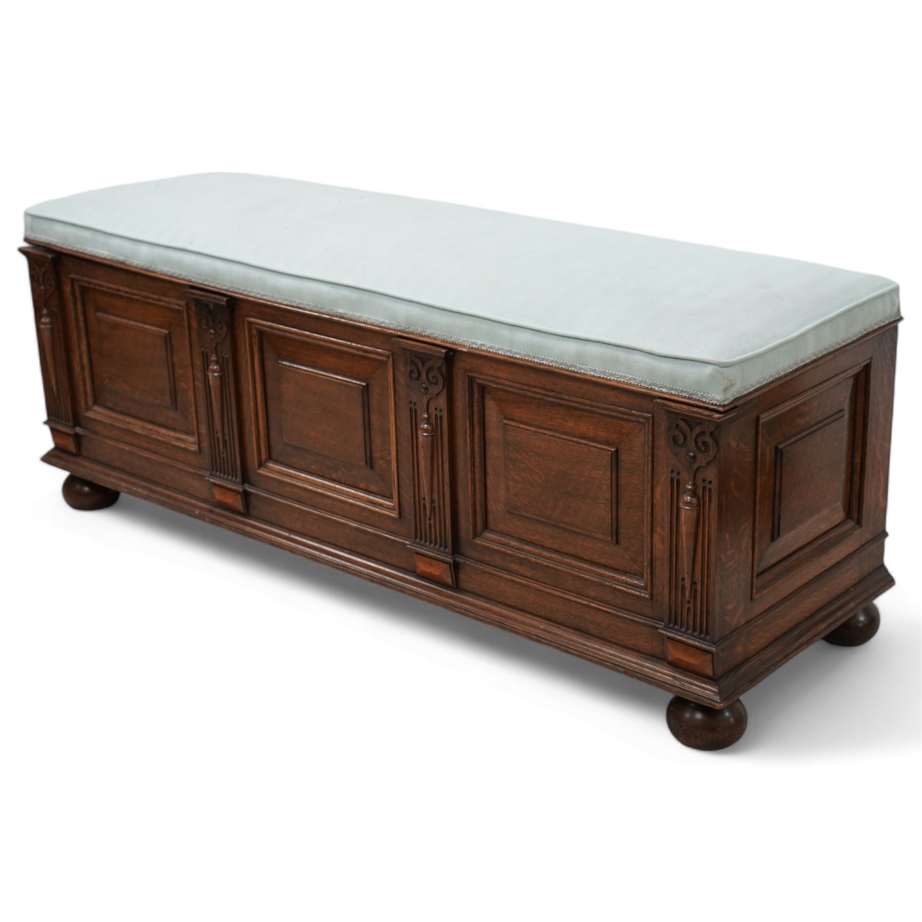 Early 20th century oak window box-seat, rectangular hinged top upholstered in blue fabric, fielded panelled front decorated with fluted and moulded uprights, raised on compressed bun feet