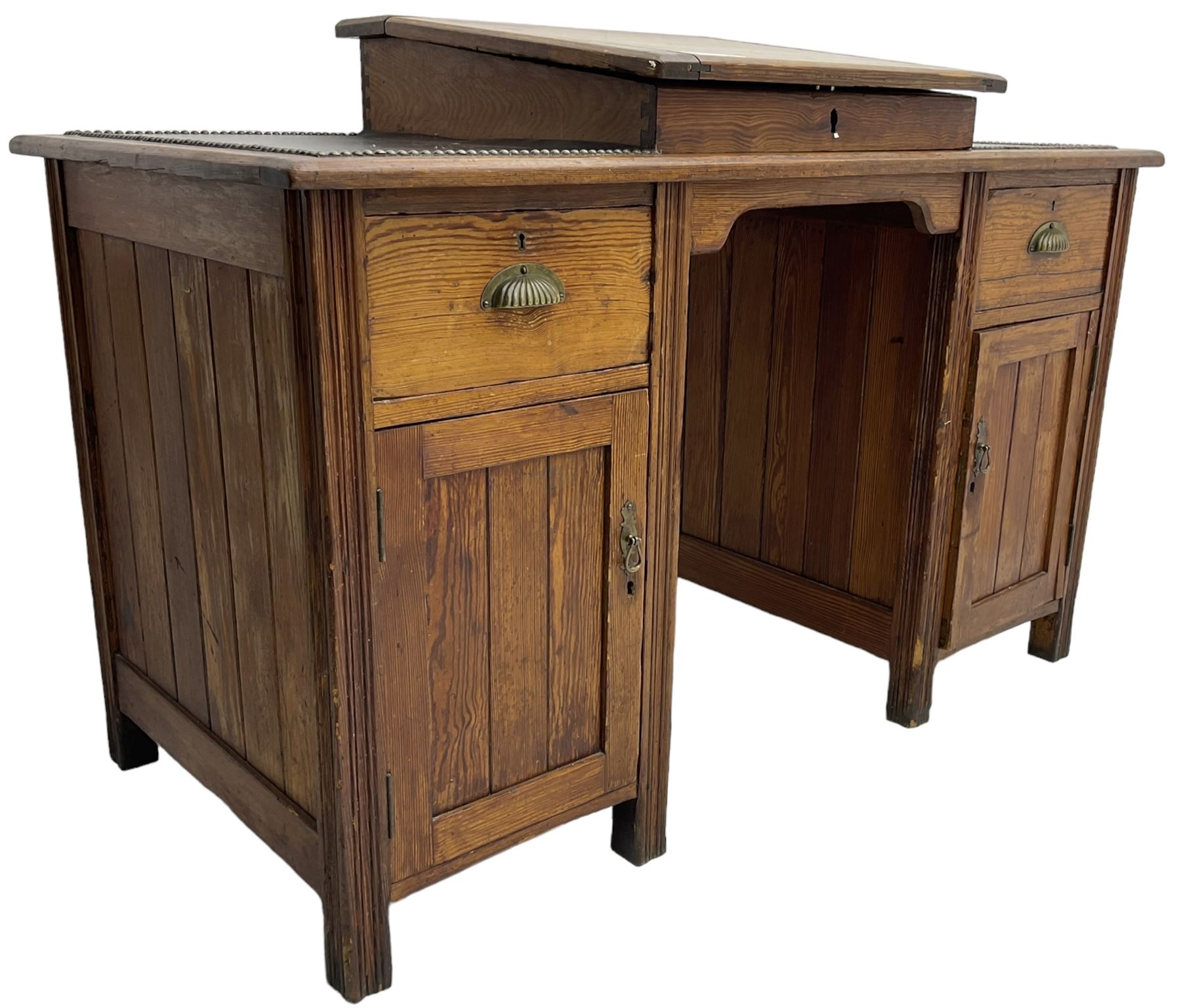 Edwardian pitch pine desk, rectangular top with writing slope flanked by inset leather writing surfaces, over twin pedestals each with shell cup handled drawer over cupboard, the left enclosing two shelves, the right enclosing sliding trays, on fluted straight supports