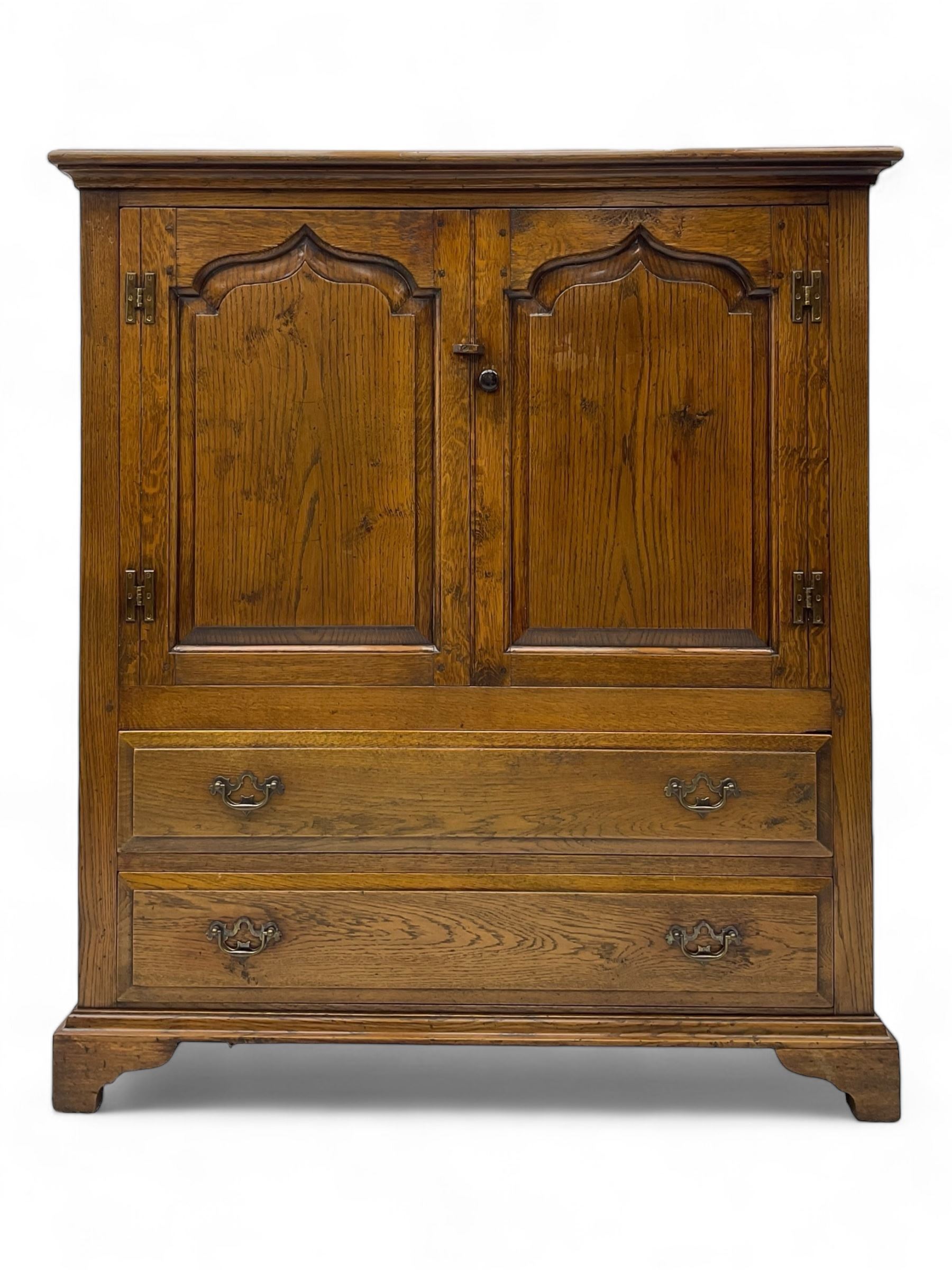 Oak drinks or media cabinet, projecting moulded cornice over two Gothic arch panelled doors on sliding tracks enclosing open storage, two drawers with brass drop handles, on bracket supports