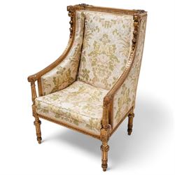 Late 19th century French gilt wood and gesso enclosed armchair, the cresting carved with floral bouquets over foliate moulding, upholstered in floral pattern fabric with repeating pattern, down-swept arms with scrolled acanthus leaf terminals, on turned and fluted feet carved with foliage 