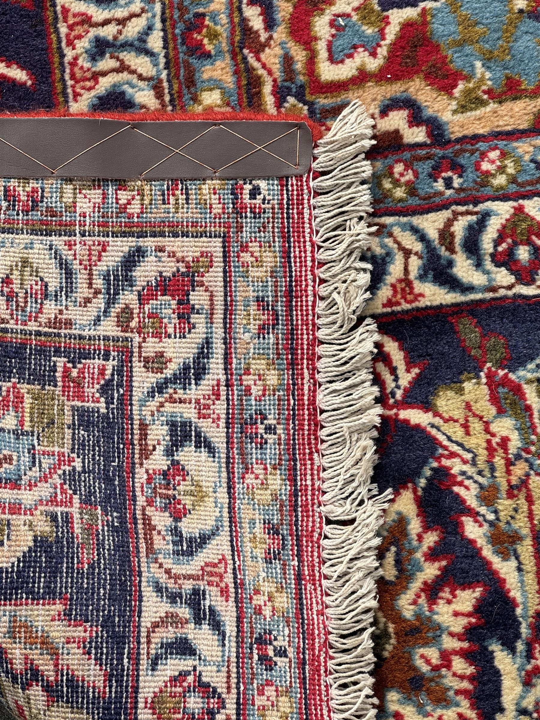 Persian Kashan red ground rug, the field decorated with a central floral medallion surrounded buy scrolling vine motifs and palmettes, the main border featuring a series of stylised floral motifs against a dark blue ground, enclosed by multiple guard stripes with alternating floral and geometric designs