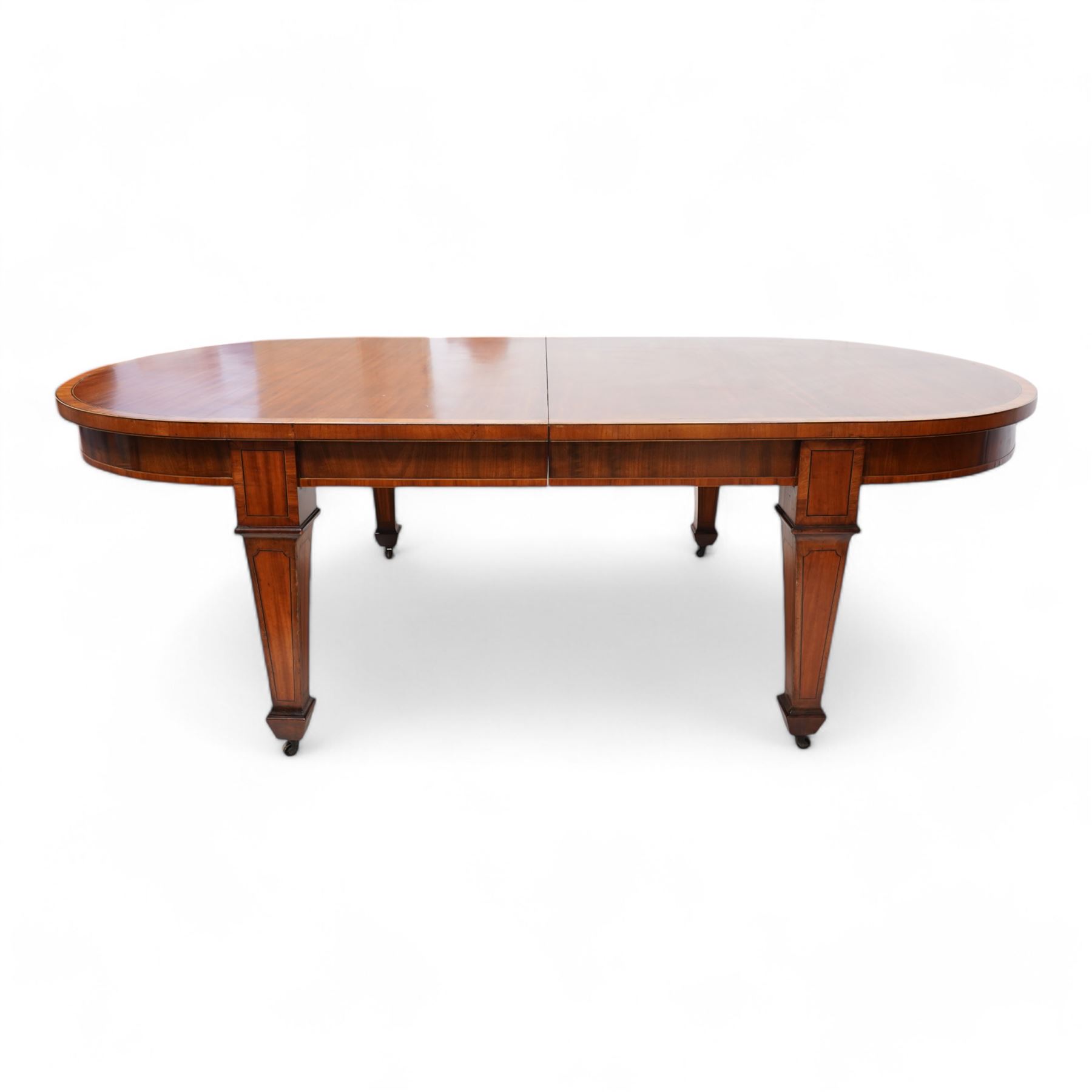 Late 19th to early 20th century mahogany and satinwood banded dining table, telescopic extending action, with three additional leaves, figured frieze rails over square tapering supports with spade feet, inlaid with satinwood panels, on brass castors 