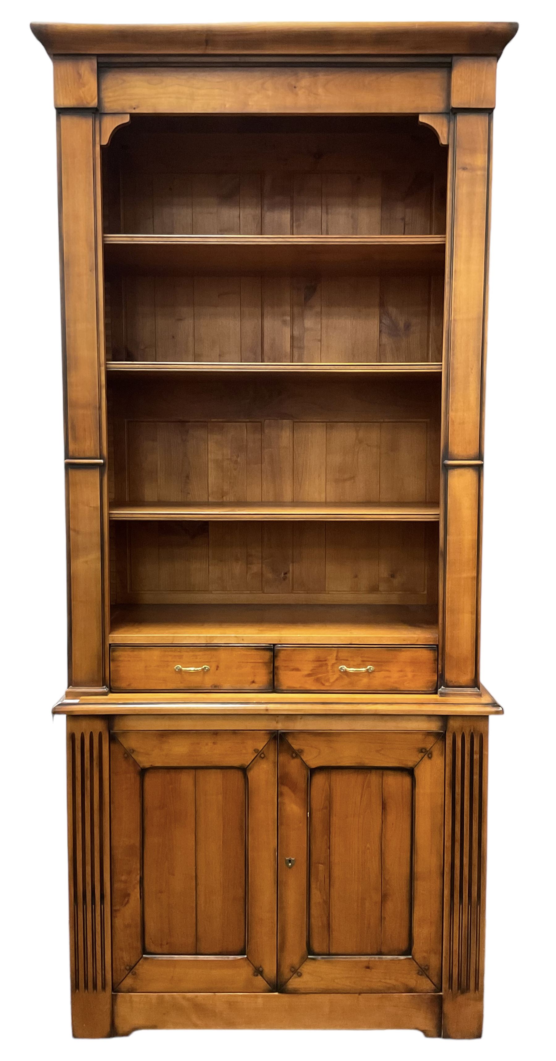 French cherry wood bookcase on cupboard, projecting moulded cornice over three shelves and two small drawers, the cupboard enclosed by two panelled doors flanked by fluted uprights