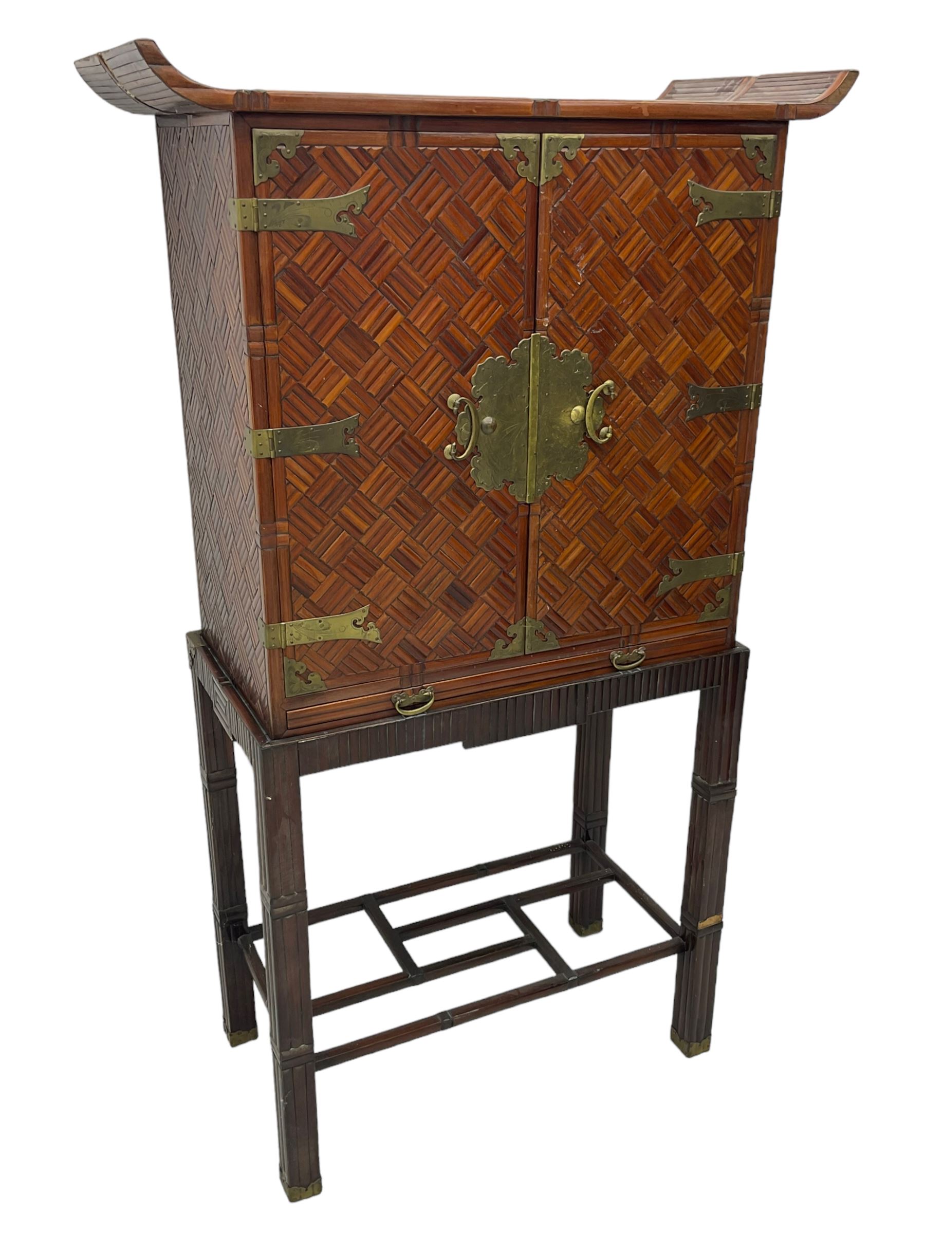 Chinese design bamboo and wood altar cabinet on stand, parquetry lattice-work bamboo, two doors with engraved metal fixtures enclosing drawers and shelf, fitted with slide, the stand pm square supports joined by a series of geometric stretchers