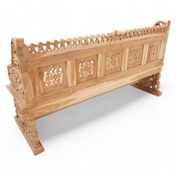 Hand carved teak garden bench, C-scroll and foliate carved cresting rail over four pierced and flower head carved panels, shaped and scrolling end supports carved with flower heads and curling leafy branches, united by pegged stretcher