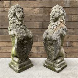 Pair of cast stone seated garden lions with shields, on stepped plinth base