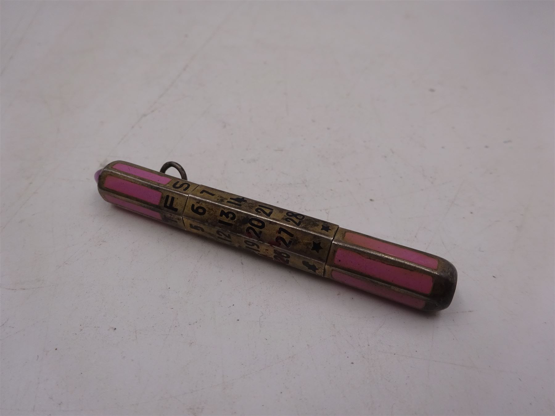 1920s silver and enamel calendar pencil, the silver faceted body decorated with panels of pink enamel with central adjustable calendar to centre, set with purple polished stone to one end, with London import marks for 1927, Cohen & Charles, L6.5cm