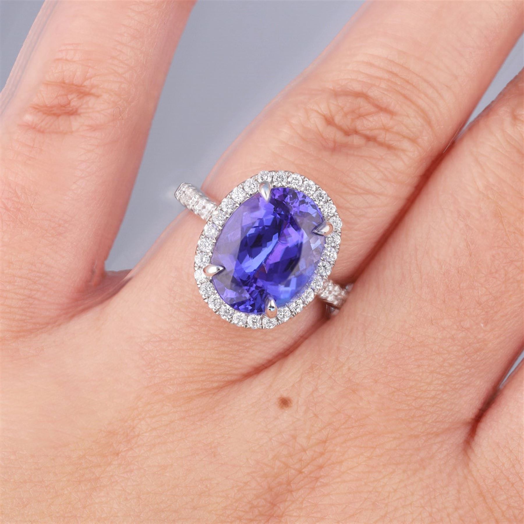 18ct white gold oval cut tanzanite and round brilliant cut diamond cluster ring, with diamond set shoulders, hallmarked, tanzanite 5.83 carat, total diamond weight 0.54 carat