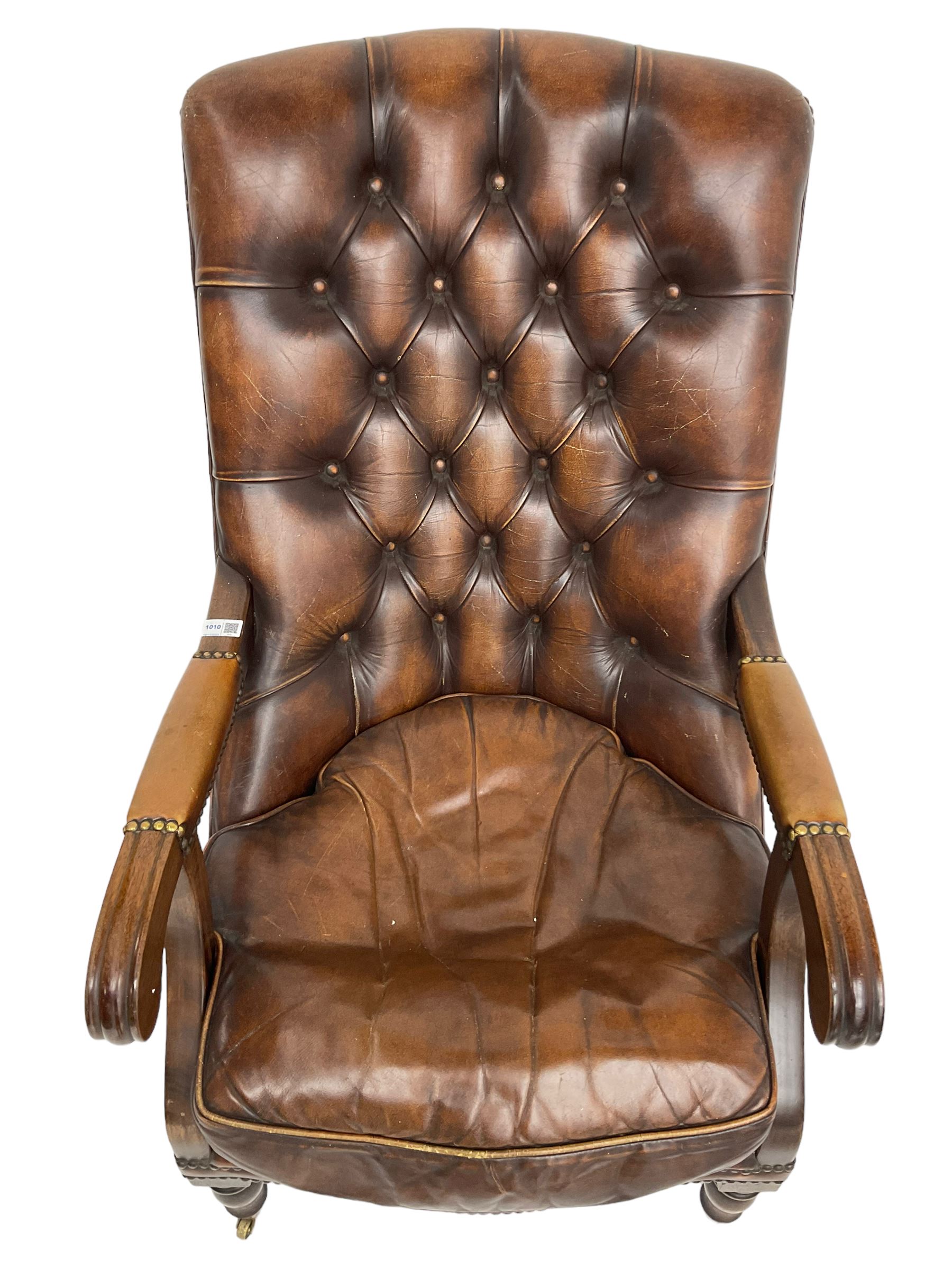 Georgian design mahogany framed library armchair, upholstered in buttoned chocolate brown leather with studwork and loose seat cushion, raised on turned supports with brass castors