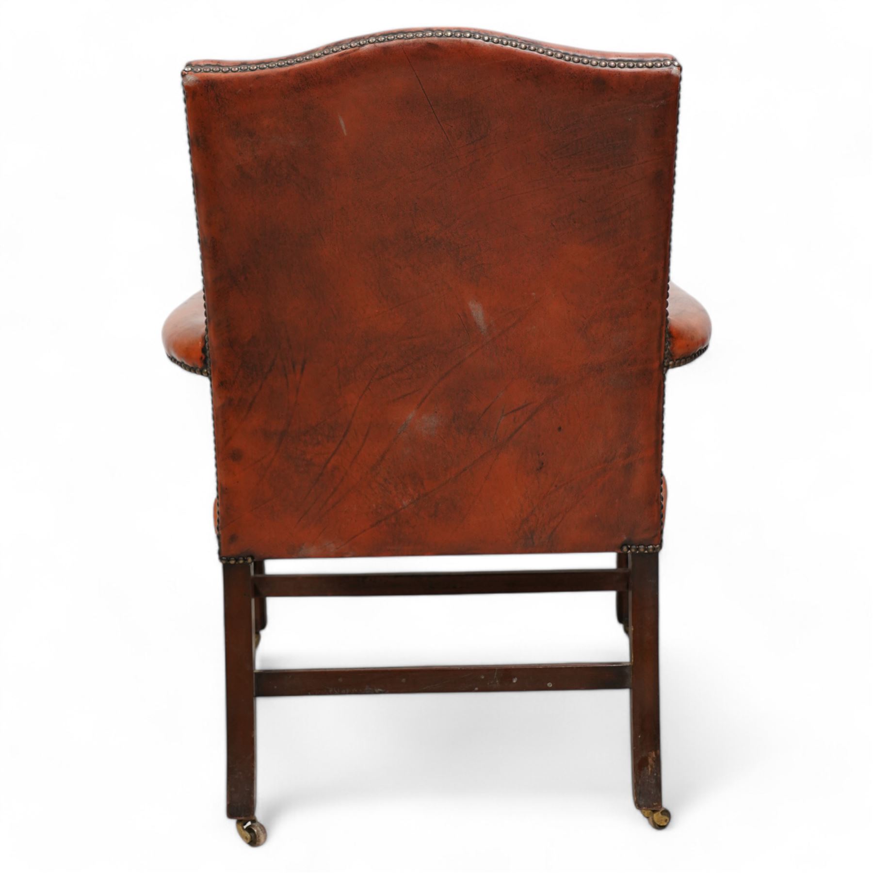 Georgian design Gainsborough elbow chair, upholstered in leather with studwork bands, moulded square supports united by H-stretcher, on brass castors 