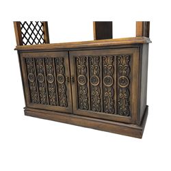 Mid 20th century oak bookcase cupboard, projecting cornice over three open shelves with subdivided sections and latticework uprights, two doors to the base with floral and scrollwork carvings and central brass handles, resting on a moulded plinth base