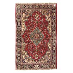 Central Persian Isfahan crimson ground carpet, central floral medallion in ivory and blue, set within a field of dense floral patterns, bordered by a navy band decorated with stylised flower heads and vines