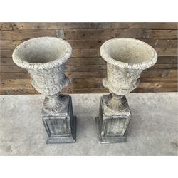 Pair of Georgian design cast stone garden urns, egg and dart rim with raised floral motifs, pedestal base terminating on square plinth, raised on square block plinth