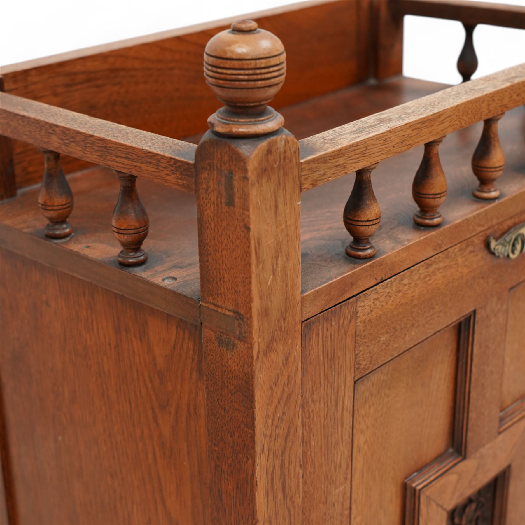 Late 19th century Aesthetic Movement walnut cupboard, raised and pierced spindle gallery surmounted by ring-turned finials, over a panelled door decorated with central foliate carved panel and surrounded by plain geometric shaped panels, applied with brass fittings and loop handle, on turned feet