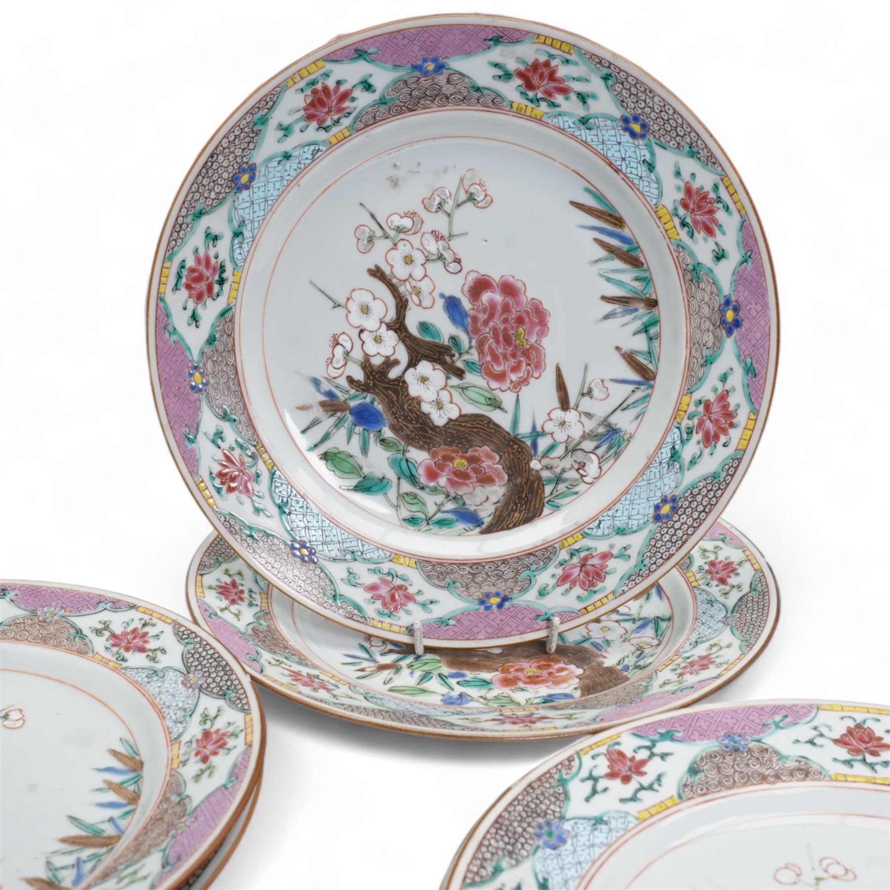 Set of nine Chinese Qianlong famille rose plates, comprising two large circular serving plates centrally enamelled with a blossoming tree branch and bamboo, within a cell diaper border, D32cm and seven side plates with matching decoration, D22.5cm 