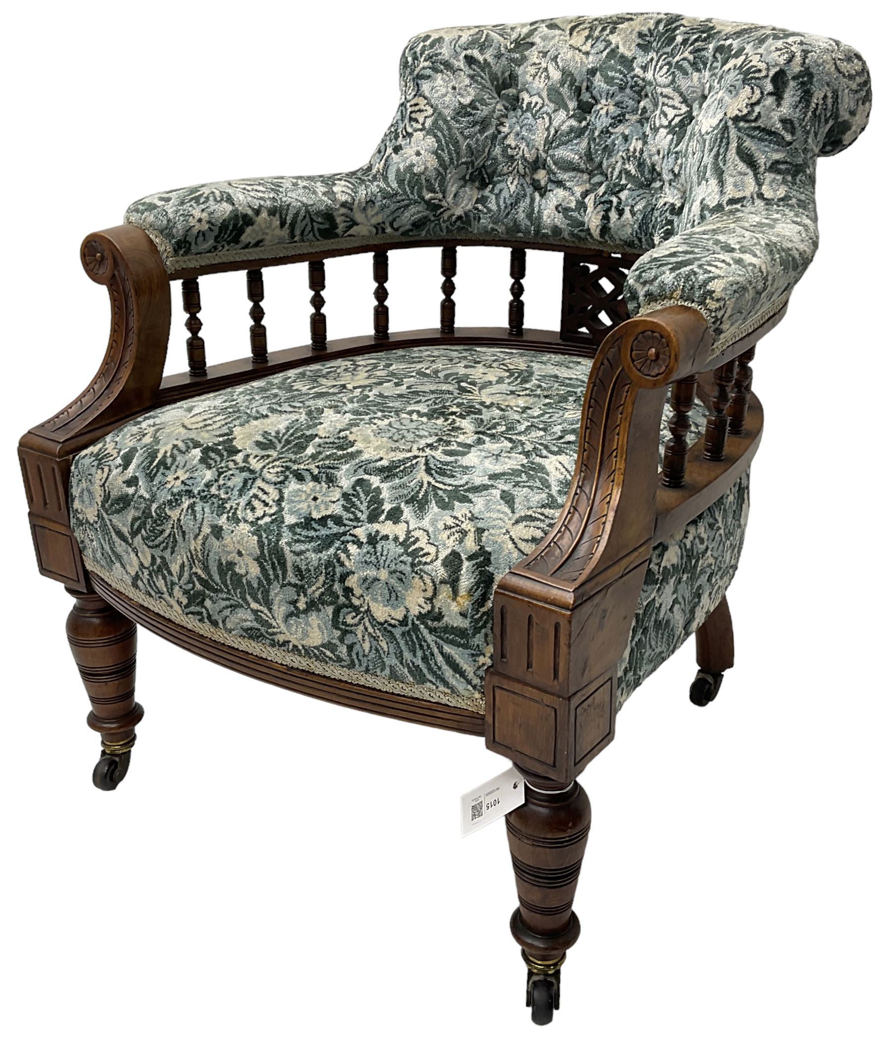 Victorian walnut framed tub-shaped armchair, the shaped rolled back supported by a spindle turned balustrade, upholstered in buttoned floral fabric, scrolled arms supports carved with acanthus leaves and flower heads, on collar turned feet with brass and ceramic castors