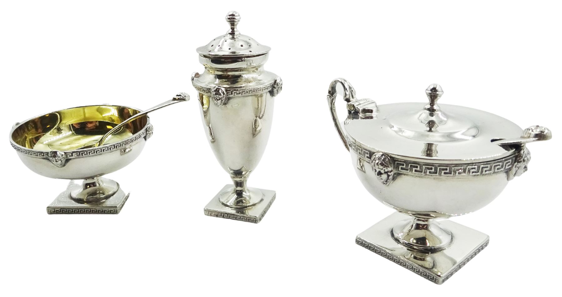 Early 20th century three piece cruet set, comprising pepper, open salt and mustard pot and cover with blue glass liner, each decorated with key fret band to rim or shoulder interspersed with female masks, and conforming key fret band to edge of square foot, together with a salt and mustard spoon, each with conforming female mask terminals, hallmarked William Hutton & Sons Ltd, Birmingham, probably 1913, and Sheffield 1923, approximate total silver weight 6.19 ozt (192.6 grams)